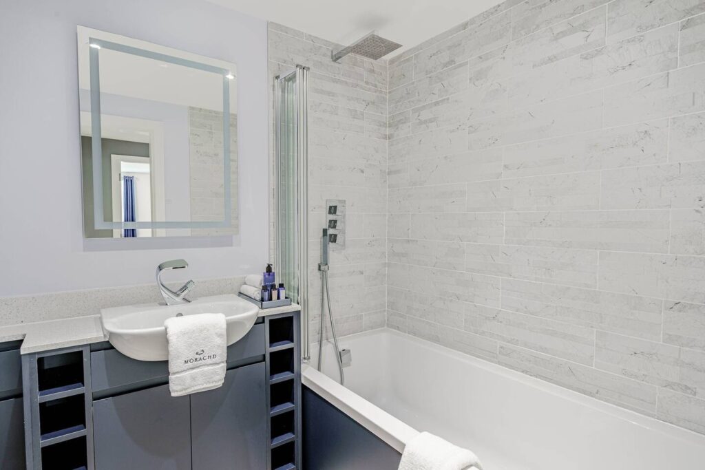 Modern bathroom with a tiled shower, white sink, mirror, and towels on the countertop.