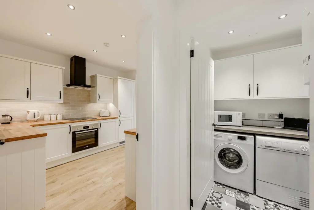 Modern kitchen and utility room with white cabinets, wooden countertops, and appliances including washing machine and microwave.