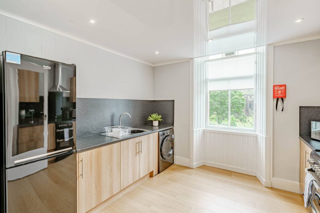 Modern kitchen with wooden cabinets, black countertops, and large window overlooking greenery.