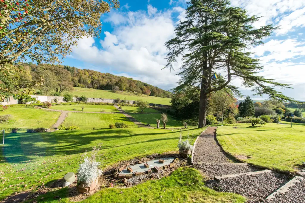 Expansive garden landscape with tree, path, and rolling hills under a blue sky. Perfect for outdoor relaxation.