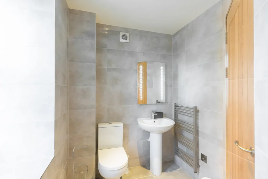 Modern bathroom with gray tiles, white toilet, pedestal sink, and metal towel rack.