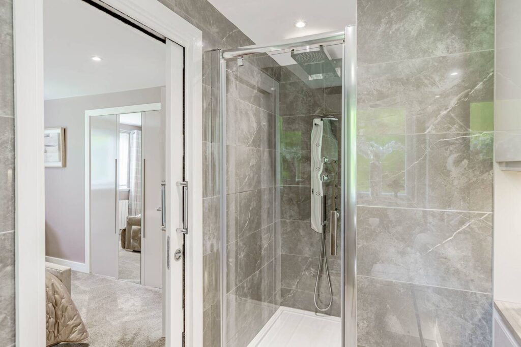 Modern bathroom with glass shower and gray marble tiles, adjacent to a cozy carpeted bedroom.