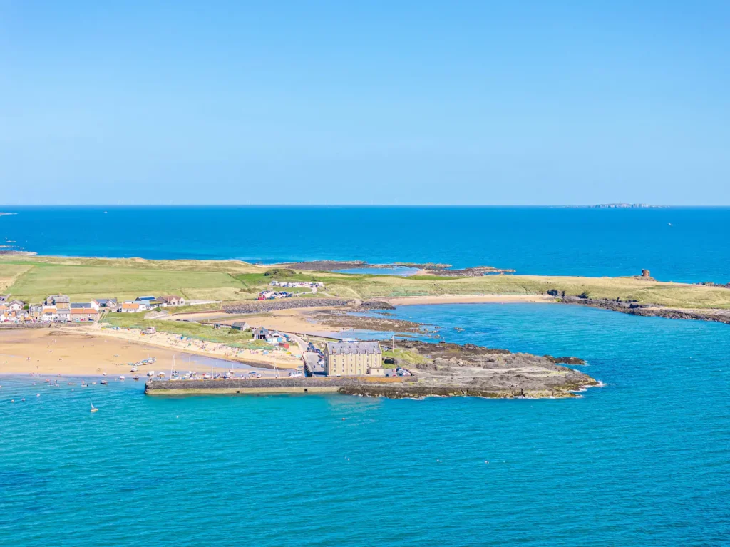 Coastal view of scenic Whitley Bay with sandy beach, trees, and blue sea under clear sky.