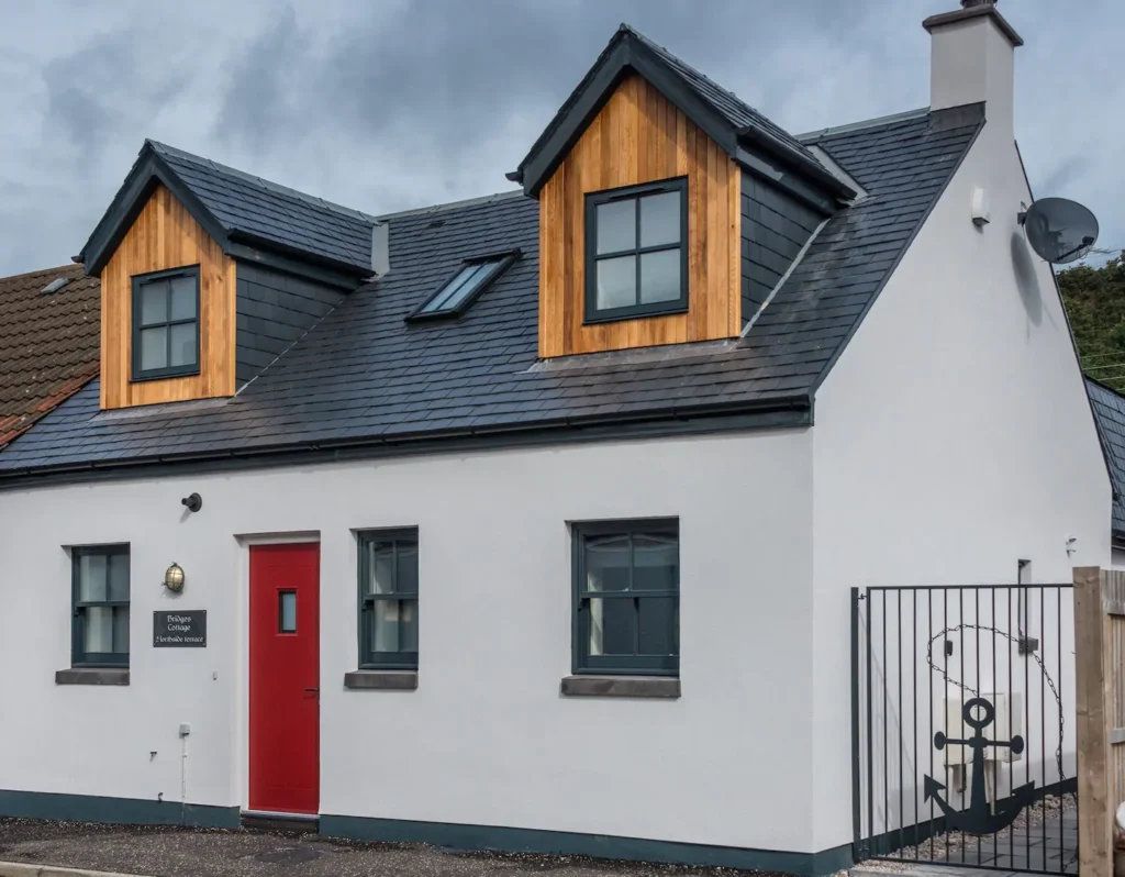 Modern white cottage with red door and nautical anchor gate design during a cloudy day.