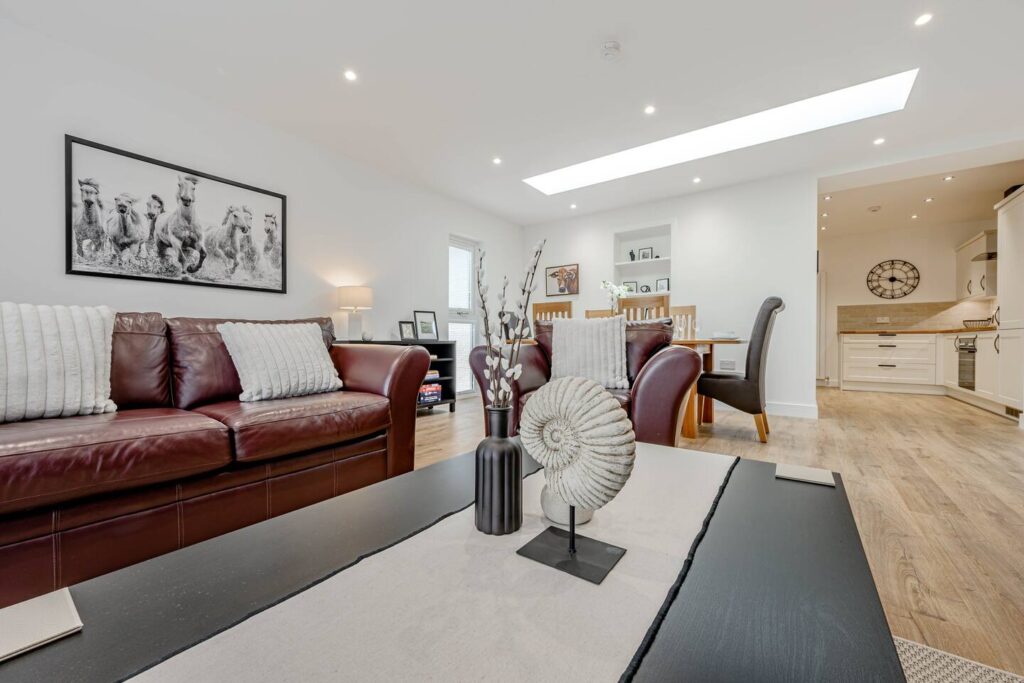 Modern open living room with leather sofa, art, and cozy dining area; bright skylight illuminates space.