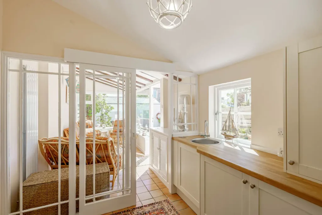 Bright kitchen and sunroom with wicker furniture and nautical decor, featuring light wood countertops and white cabinetry.