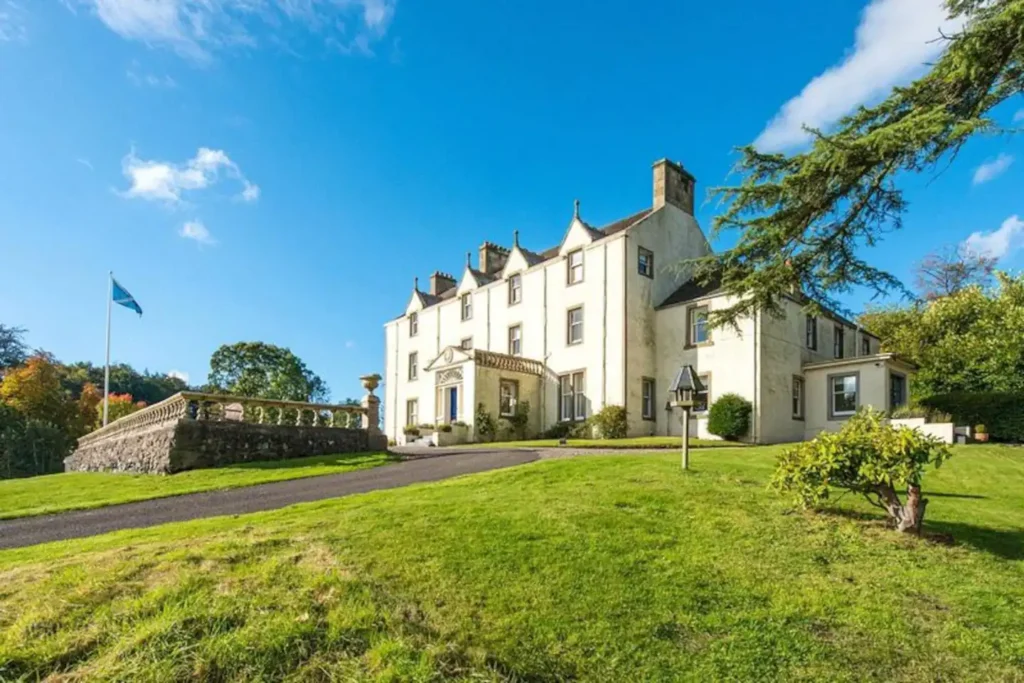 Historic mansion with lush green lawn and Scottish flag under a bright blue sky.