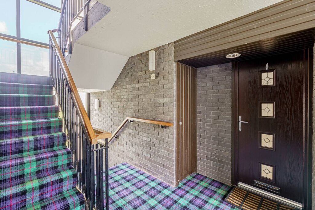 Colorful plaid carpet on stairway next to a modern dark wooden door in a well-lit building hallway.