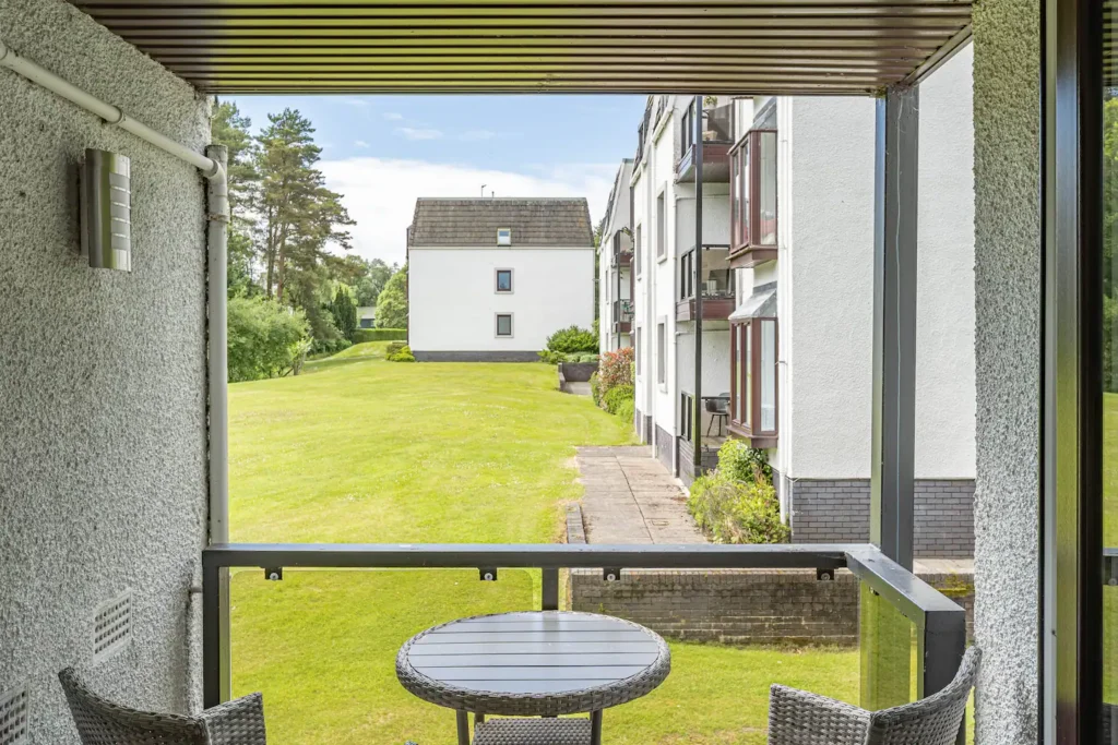 Balcony view of green lawn and residential building on a sunny day, perfect for relaxation and outdoor enjoyment.