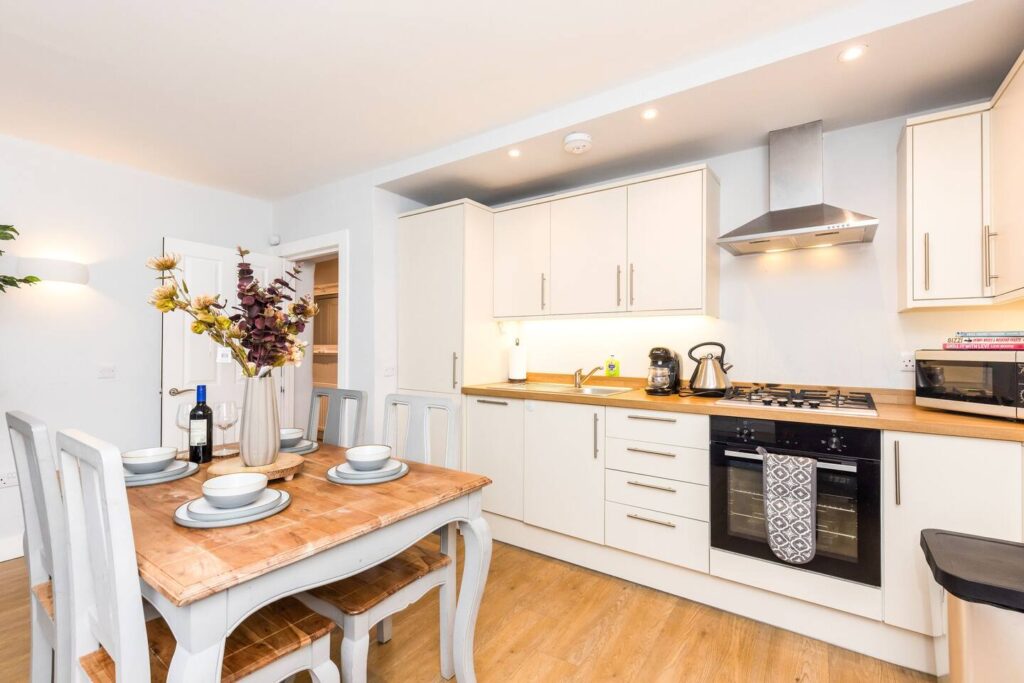 Modern kitchen with white cabinets, wooden dining table set, flowers, and stainless steel appliances.