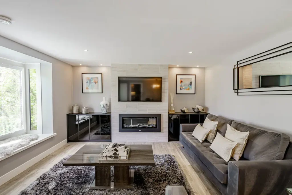 Modern living room with gray sofa, wall-mounted TV, fireplace, and decorative artwork. Cozy and stylish interior design.