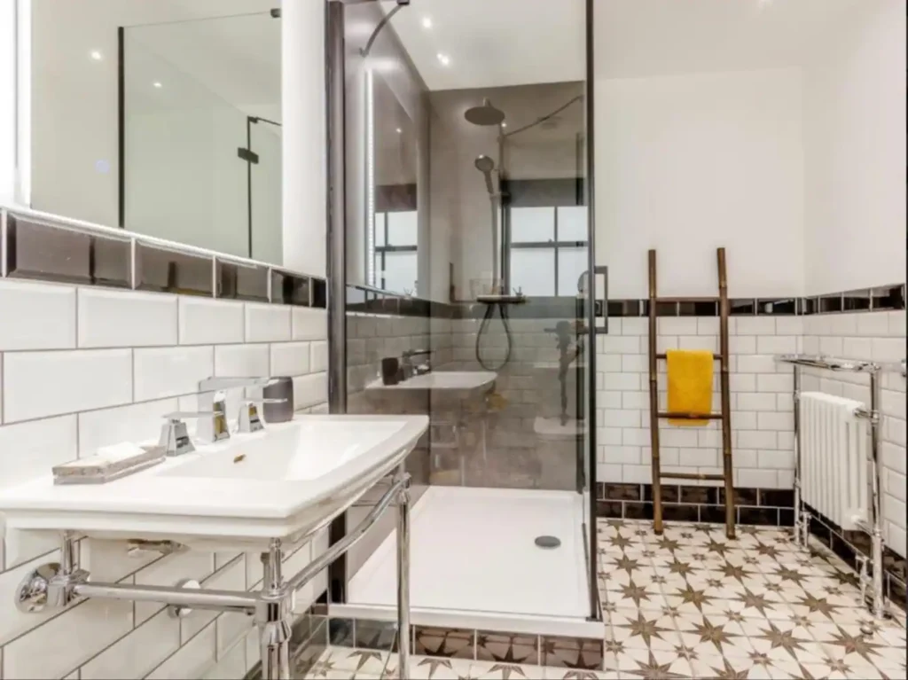 Modern bathroom with subway tiles, glass shower, patterned floor, and yellow towel on a ladder rack.