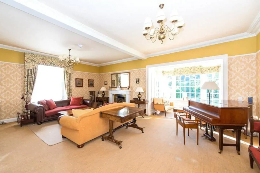 Elegant living room with vintage decor, grand piano, and cozy sofas under a chandelier in a bright, inviting space.