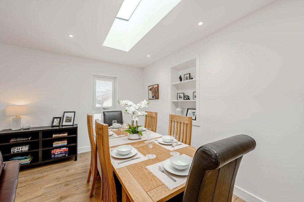 Modern dining room with wooden table, skylight, and elegant decor. Bright, airy space for gatherings and meals.