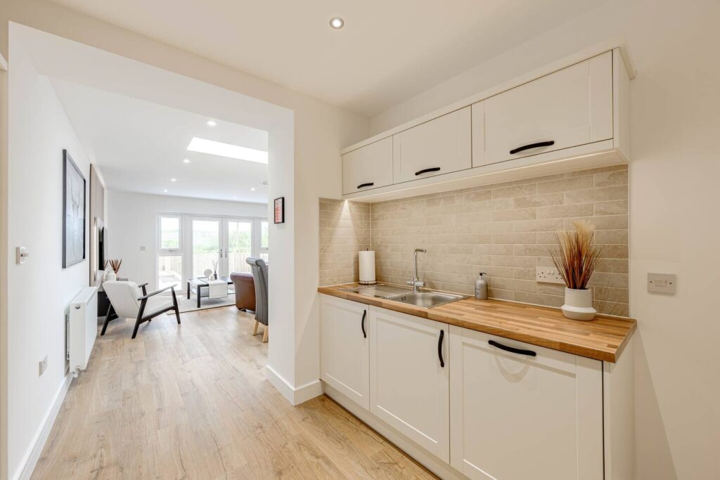 Modern kitchen with wooden countertops and open living room, featuring light wood flooring and natural light.