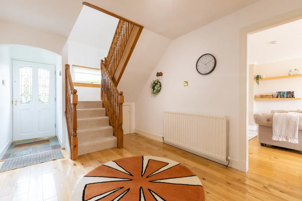 Bright wooden hallway with stairs, modern decor, and vibrant round rug near open living room.