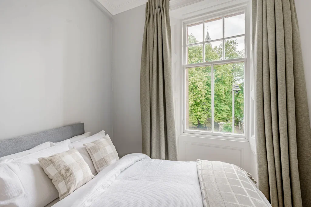 Elegant bedroom with a cozy bed, large window, and garden view. Perfect serene space for relaxation.