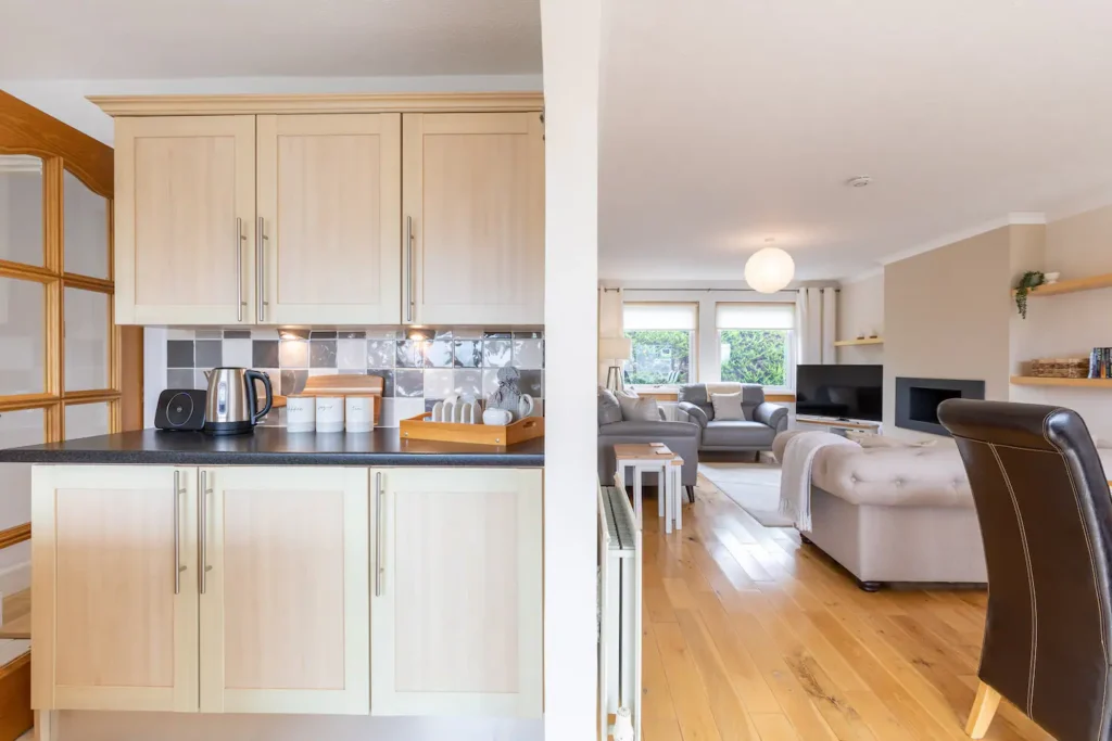 Modern kitchen and living room with light wood cabinets, cozy seating, and natural light.