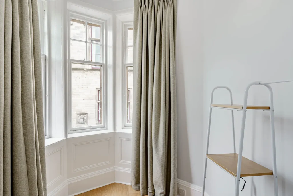 Bright corner room with beige curtains, white trim windows, and a modern white ladder shelf.