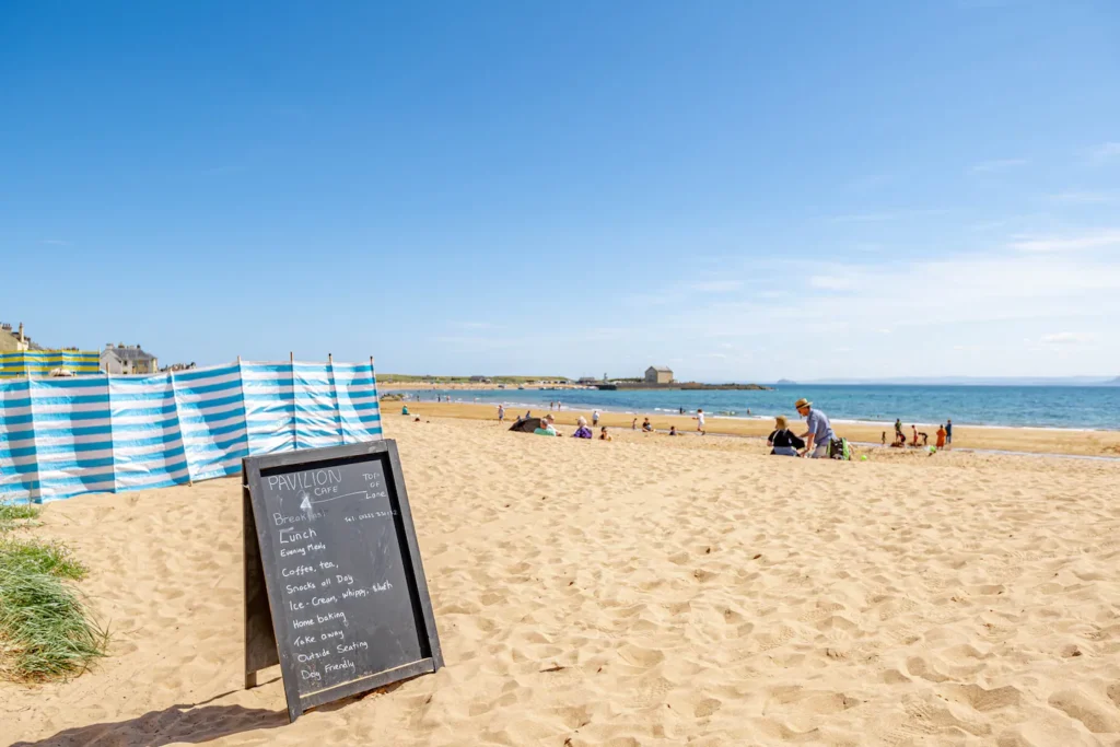 Sunny beach scene with a menu board, beachgoers, and blue sky, perfect for a summer day out.