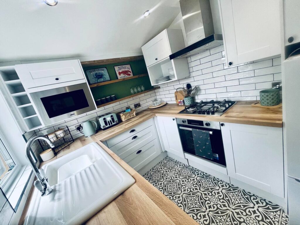 Modern kitchen with white cabinets, wooden countertops, and patterned floor tiles, featuring a gas stove and sink.