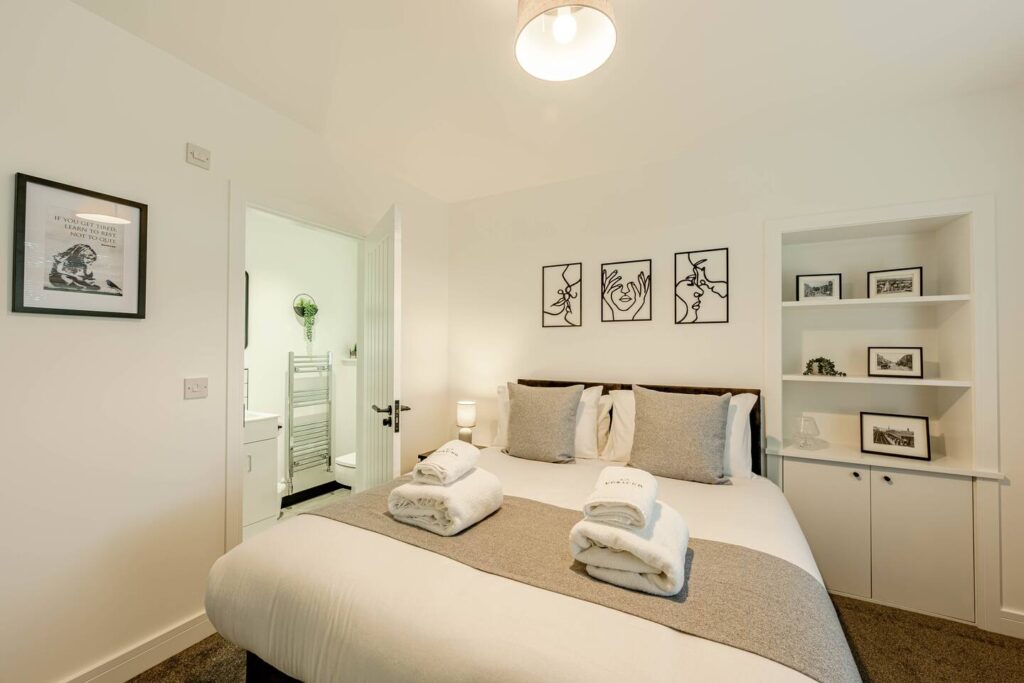 Cozy bedroom with modern decor, double bed, gray accents, and wall art, adjacent to a bright en-suite bathroom.