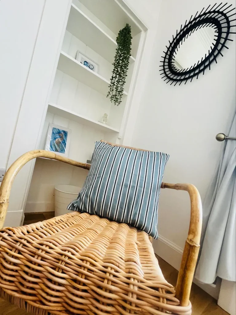 Cozy wicker chair with striped cushion in a modern living room, near a plant and decorative mirror.