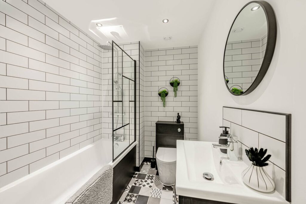 Modern bathroom with white subway tiles, round mirror, and geometric floor tiles. Elegant design with greenery accents.