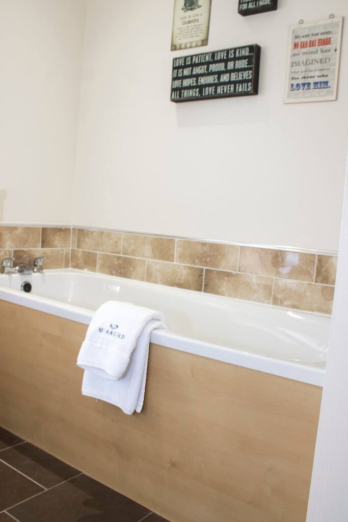 Modern bathroom with a white bathtub, beige tiles, and inspirational wall art for a relaxing ambiance.