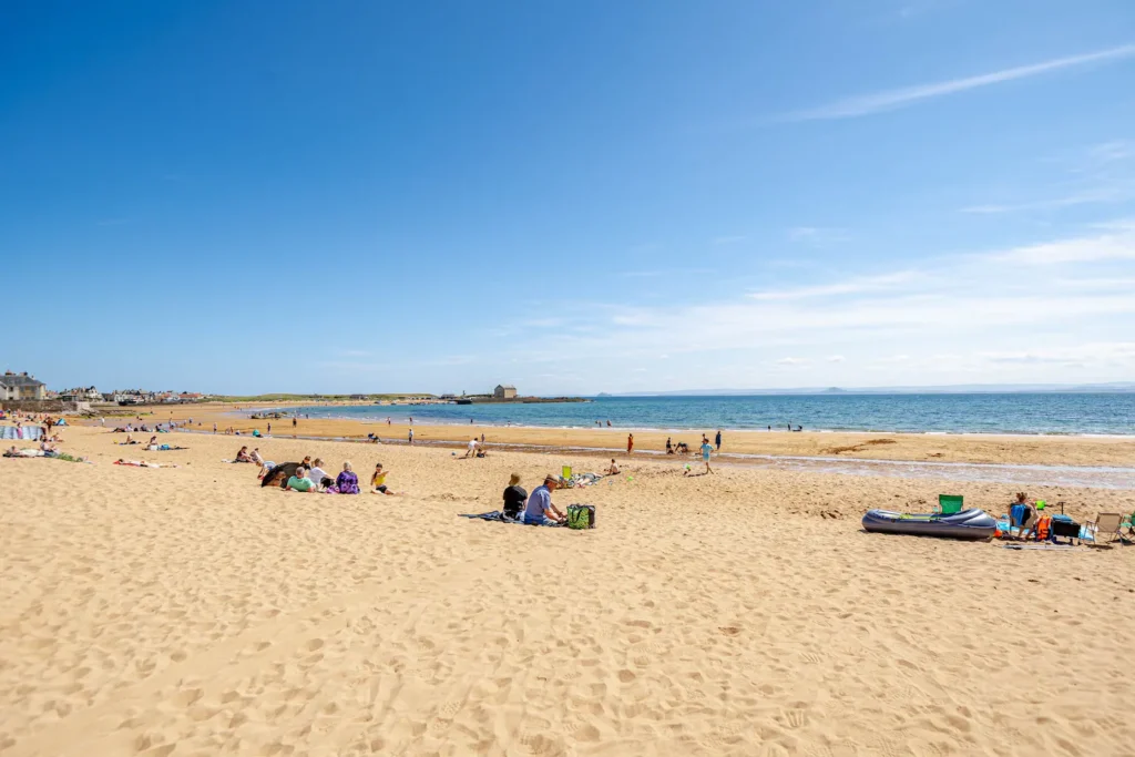 Sandy beach with people relaxing under a clear blue sky near the ocean. Perfect summer day at the seaside.