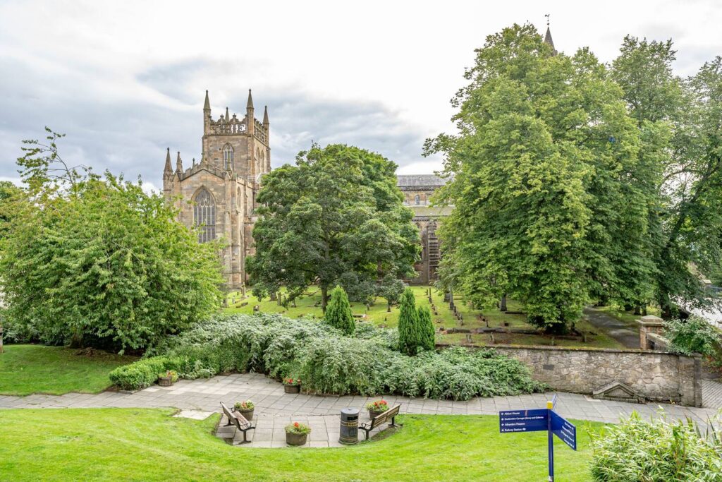 Historic stone cathedral surrounded by lush green trees and a serene garden path.