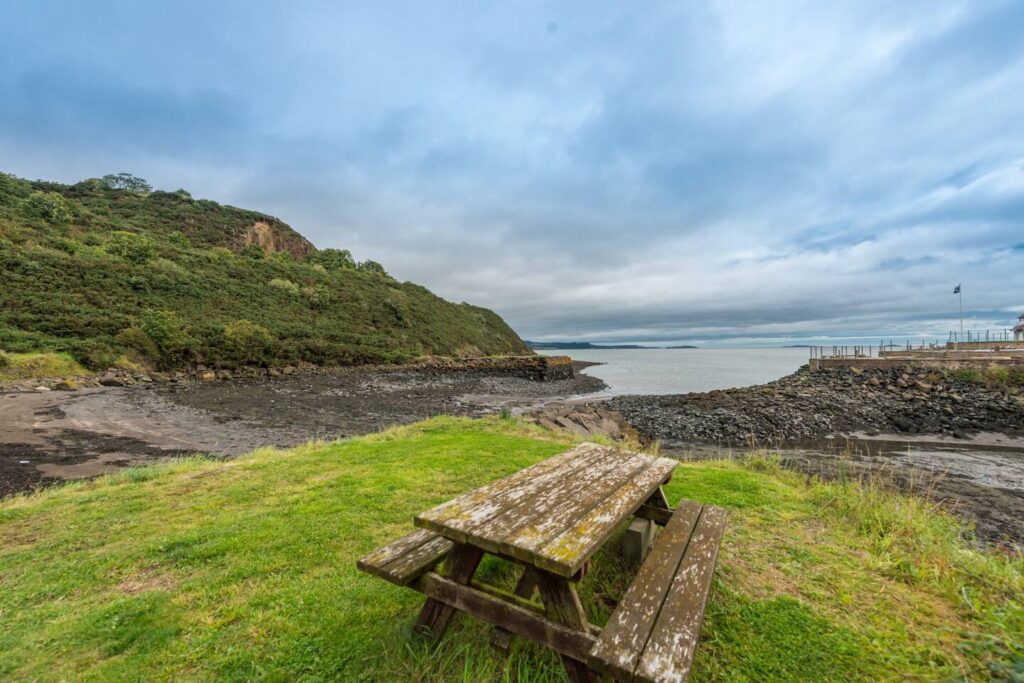 Weathered picnic table overlooking scenic seaside cliffs and calm waters under a cloudy sky.