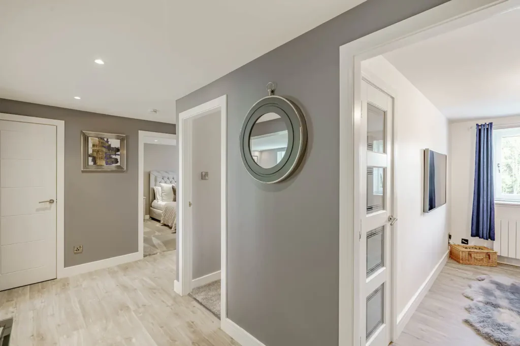 Modern hallway with gray walls and bedroom view, featuring a circular mirror and decor.