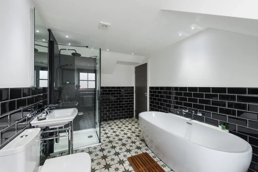 Modern bathroom with black tiles, glass shower, and freestanding tub on patterned floor. Stylish interior design.