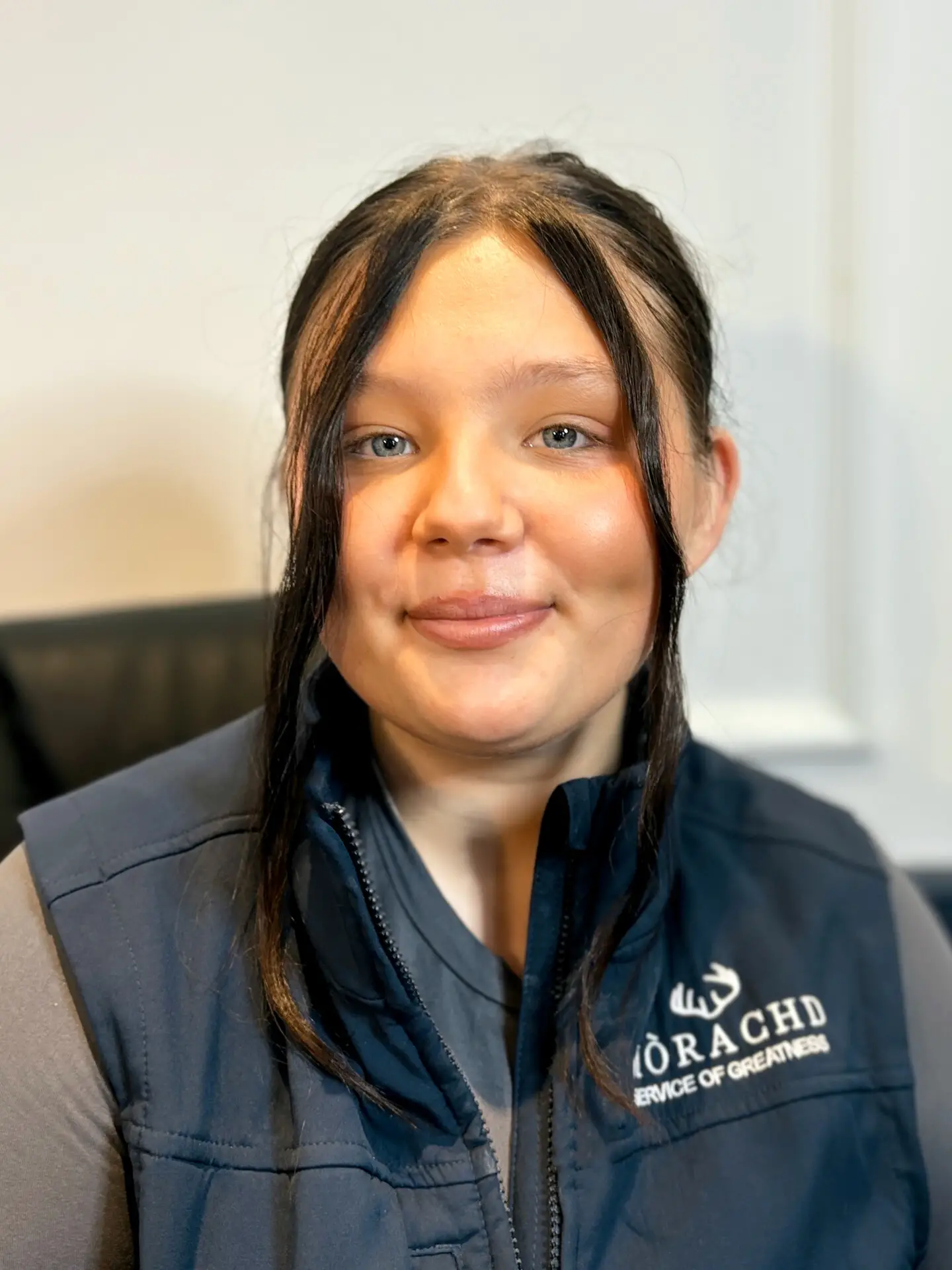 Woman in a navy vest smiles at the camera against a neutral background.